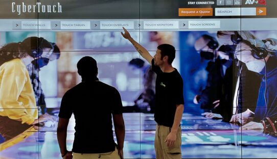 Man showing another man how to use an interactive touchscreen display in a New Orleans office
