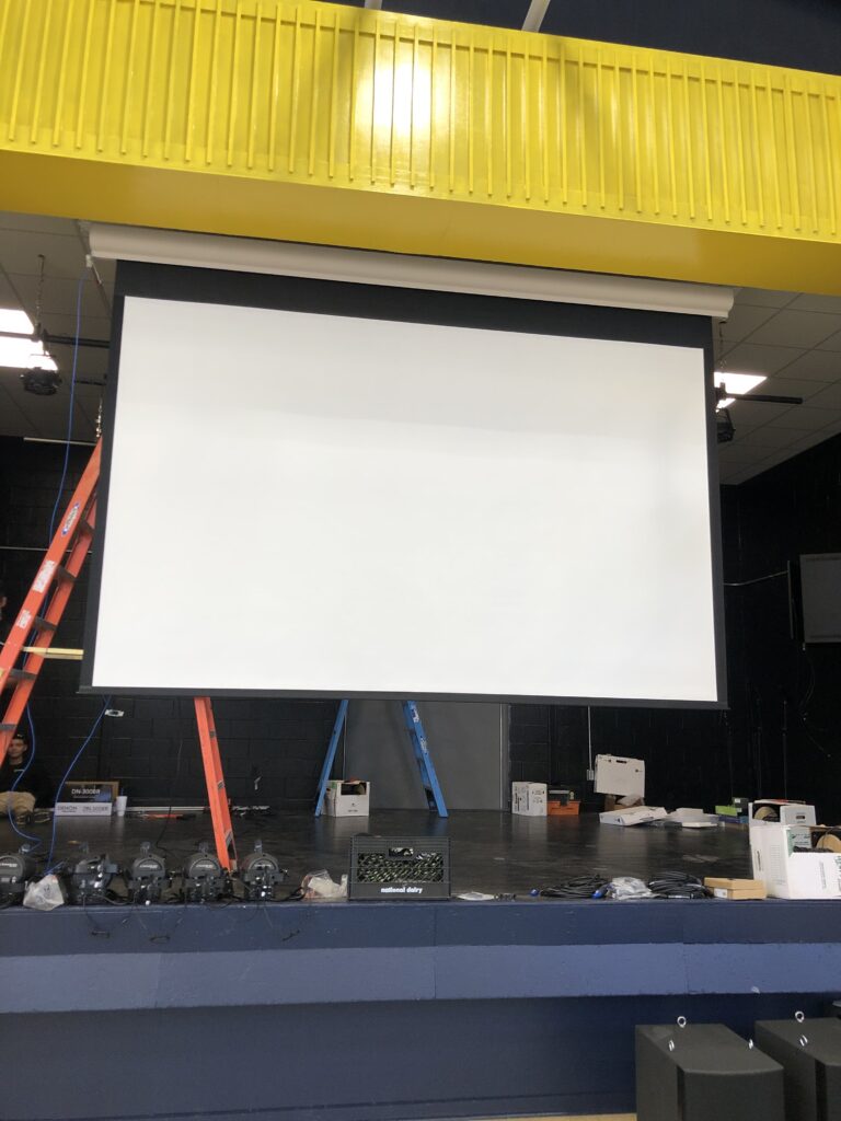 Large projection screen installed on a school stage for audiovisual presentations
